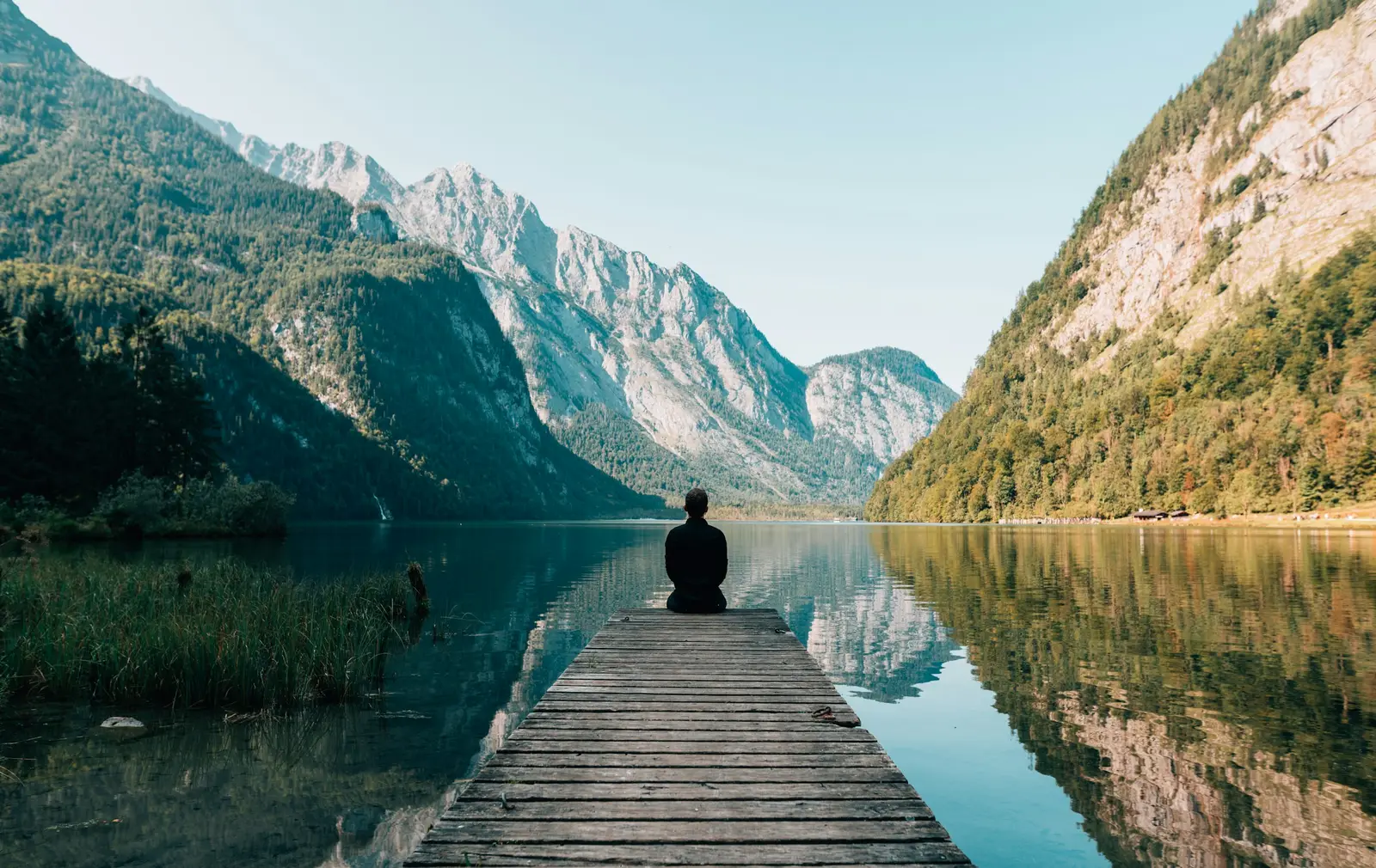 Jemand springt mit ausgebreiteten Armen an einem Bergsee
