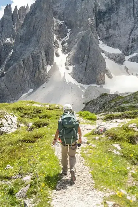 Eine Wanderin geht von hinten gesehen einen Bergweg in den Dolomiten entlang