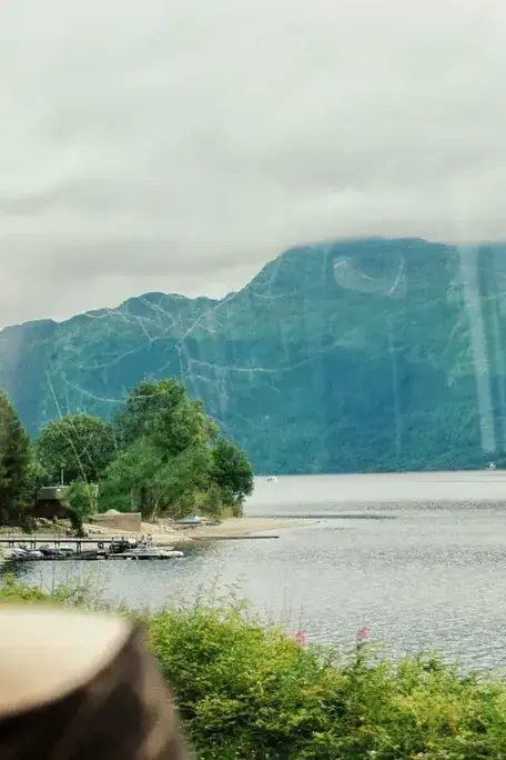Blick aus einem Zugfenster auf einen See und bewaldete Berge